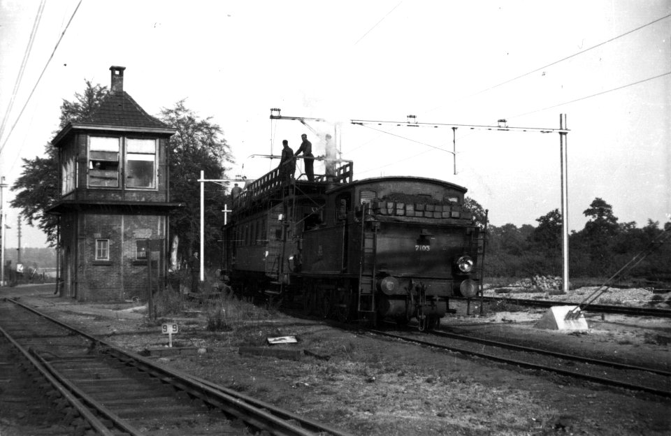 HUA-160424-Afbeelding van de stoomlocomotief nr. 7103 (serie 7100) van de N.S. met een bovenleidingsmontagewagen, tijdens de electrificatie van het rangeerterrein te Susteren. Links een seinhuis