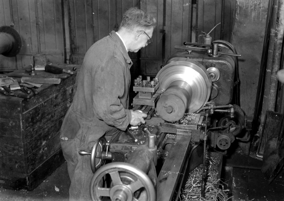 HUA-167432-Afbeelding van de gepensioneerde draaier Brekelmans in de Centrale Werkplaats van de N.S. te Tilburg tijdens het draaien van een buffer voor een oude N.R.S.-stoomlocomotief van het Spoorwegmuseum