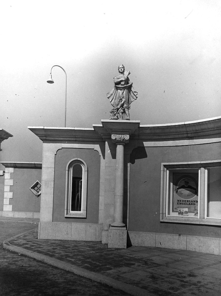 HUA-163874-Gezicht op een gedeelte van het reisbureau in de linkervleugel van het vernieuwde N.S.-station Gouda te Gouda, met op de daklijst één van de vier door Jo Uiterwaal vervaardigde beelden "De Vier Indust