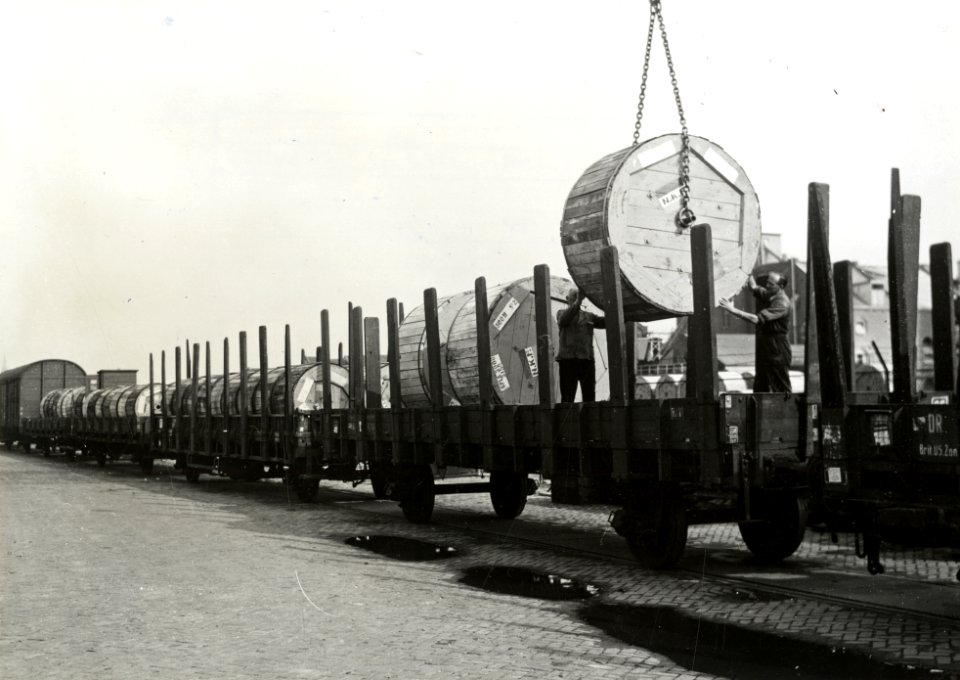 HUA-167307-Afbeelding van het beladen van rongenwagens met haspels met kabels van de N.K.F. (Nederlandse Kabelfabriek) op de laad- en losplaats van het N.S.-station Delft te Delft