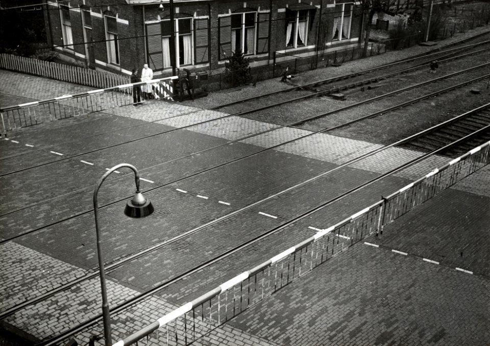 HUA-167402-Gezicht op de spoorwegovergang in de Stationsweg - Bennekomseweg (noordelijke sporen) bij het N.S.-station Ede-Wageningen te Ede, met gesloten overwegbomen en de voormalige opzichterswoning