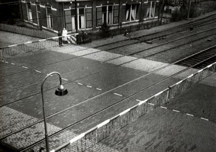 HUA-167402-Gezicht op de spoorwegovergang in de Stationsweg - Bennekomseweg (noordelijke sporen) bij het N.S.-station Ede-Wageningen te Ede, met gesloten overwegbomen en de voormalige opzichterswoning