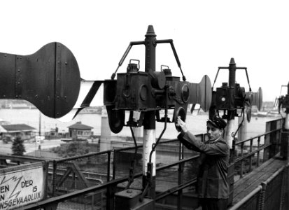 HUA-163923-Afbeelding van Wim Kan van het ABC-Cabaret op de seinbrug bij het N.S.-station Amsterdam C.S. te Amsterdam, tijdens het poetsen van de glazen in de seinarmen. N.B. De foto is gemaakt in het kader van 