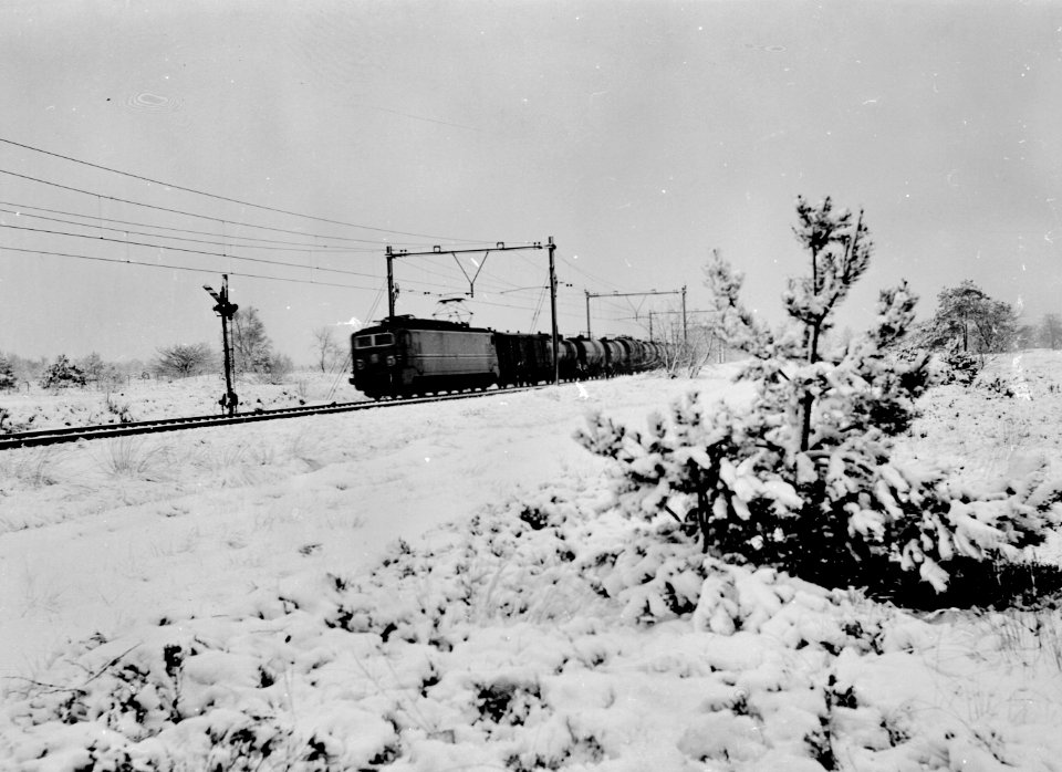 HUA-167382-Afbeelding van een goederentrein (olietrein), getrokken door een electrische locomotief uit de serie 1300 van de N.S. in een besneeuwd landschap