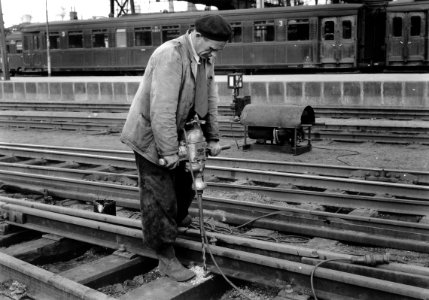 HUA-167443-Afbeelding van een wegwerker van de NS met een boormachine met aggregaat tijdens het boren van gaten in dwarsliggers voor de montage van de hellingpla