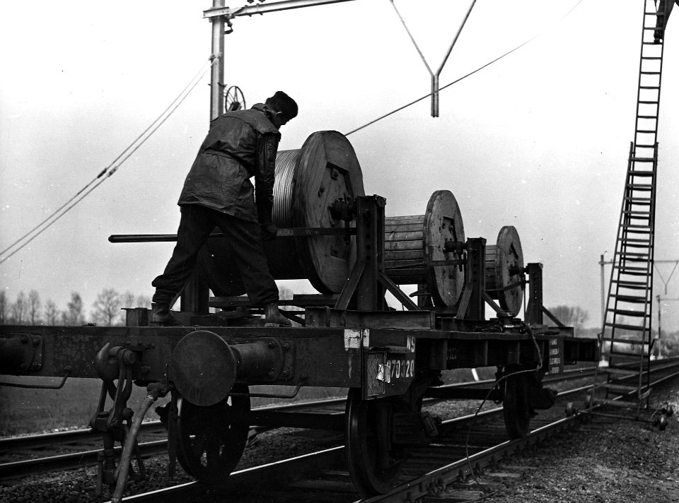 HUA-164031-Afbeelding van een monteur op een haspelwagen van de N.S. tijdens het "draadtrekken" voor de bovenleiding op de spoorlijn tussen Dieren en Brummen, ten behoeve van de electrificatie van de lijn Arnhem