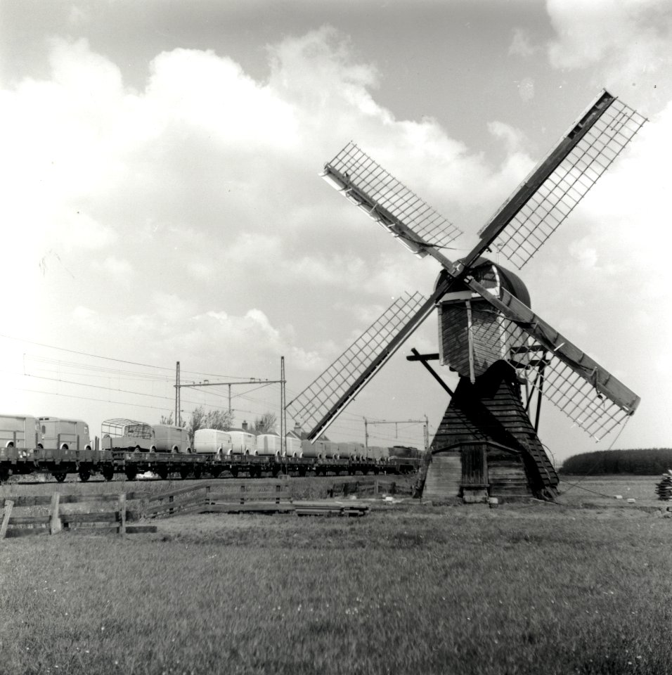 HUA-167017-Afbeelding van een passerende goederentrein beladen met bestelauto s ter hoogte van Lisse met op de voorgrond een wipwatermolen