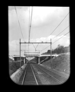 HUA-167173-Gezicht op de spoorlijn tussen Ede en Arnhem, vanuit een rijdende trein, met het viaduct in Rijksweg 12 tussen Ede-Wageningen en Wolfheze