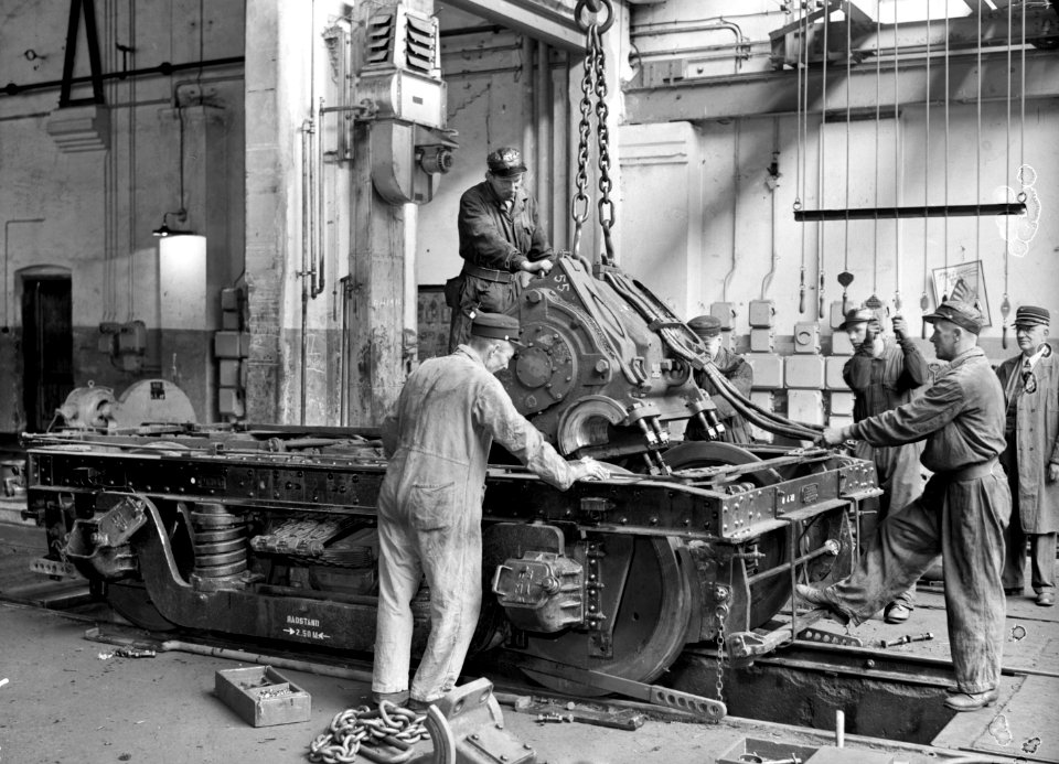 HUA-159369-Interieur van de revisieloods (werkplaats) van de N.S. te Leidschendam tijdens het plaatsen van een tractiemotor in een draaistel van een electrisch motorrijtuig mnat. 1924 ("blokkendozen")
