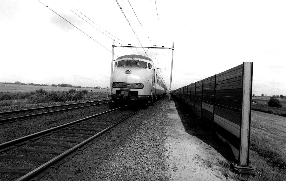 HUA-167176-Afbeelding van de proefopstelling van een geluidsscherm langs de spoorlijn ten westen van Woerden (nabij Oudewater), met een passerende trein bestaande uit electrische treinstellen mat. 1964 (plan V) 