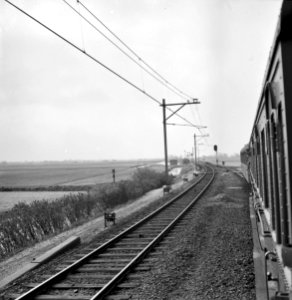 HUA-167166-Gezicht op de spoorlijn nabij Noord Scharwoude vanuit een rijdende trein waarbij slechts één spoor voorzien is van bovenleiding