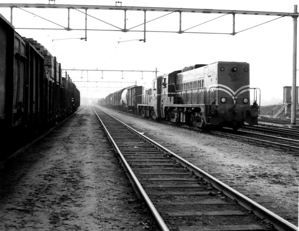 HUA-166561-Afbeelding van de diesel-electrische locomotief nr. 2203 (serie 2200-2300) van de N.S. met een goederentrein op het emplacement te Nijmegen