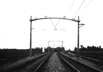 HUA-163775-Gezicht op de juist geëlectrificeerde spoorlijn met betonnen bovenleidingsportalen in de omgeving van Lage Zwaluwe