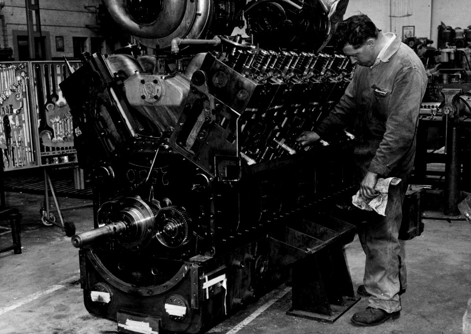 HUA-159404-Afbeelding van een monteur van de hoofdwerkplaats van de N.S. te Tilburg bij een SACM MGO V12-dieselmotor voor een diesel-electrische locomotief uit de serie 2400-2500 (nr. 2530?) van de N.S