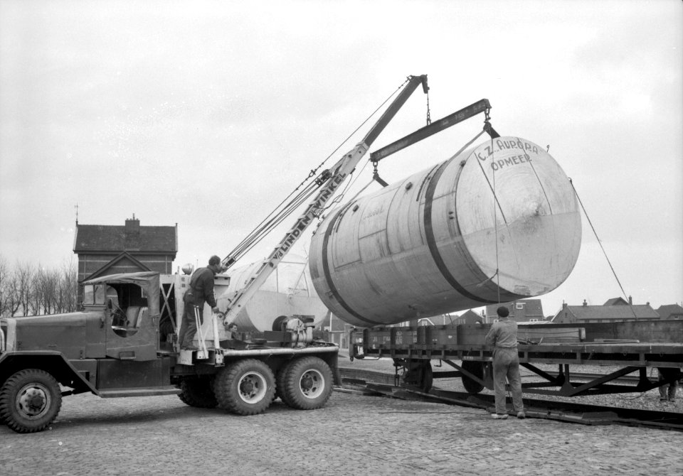 HUA-167006-Afbeelding van het overladen van een melkketel van de Coöperatieve Zuivelfabriek Aurora te Opmeer van een platte goederenwagen naar een vrachtauto op de laad- en losplaats van het N.S.-station Obdam t