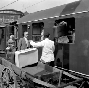 HUA-166725-Afbeelding van een kruier tijdens het inladen van de bagage in een trein langs het perron van het N.S.-station Arnhem te Arnhem