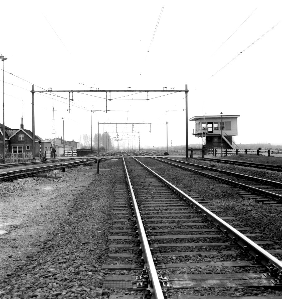 HUA-167136-Afbeelding van de zuidzijde van het emplacement van het N.S.-station Elst te Elst (Elst aansluiting), gezien in de richting Nijmegen, met de spoorwegovergang in de Bemmelseweg en het seinhuis Post T