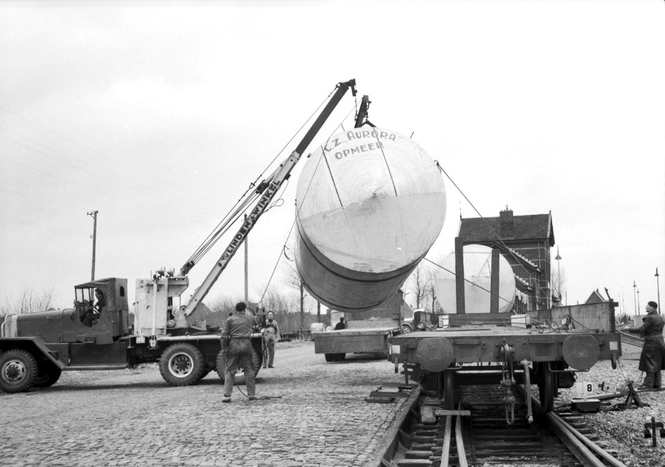 HUA-167010-Afbeelding van het overladen van een melkketel van de Coöperatieve Zuivelfabriek Aurora te Opmeer van een platte goederenwagen naar een vrachtauto op de laad- en losplaats van het N.S.-station Obdam te Obdam