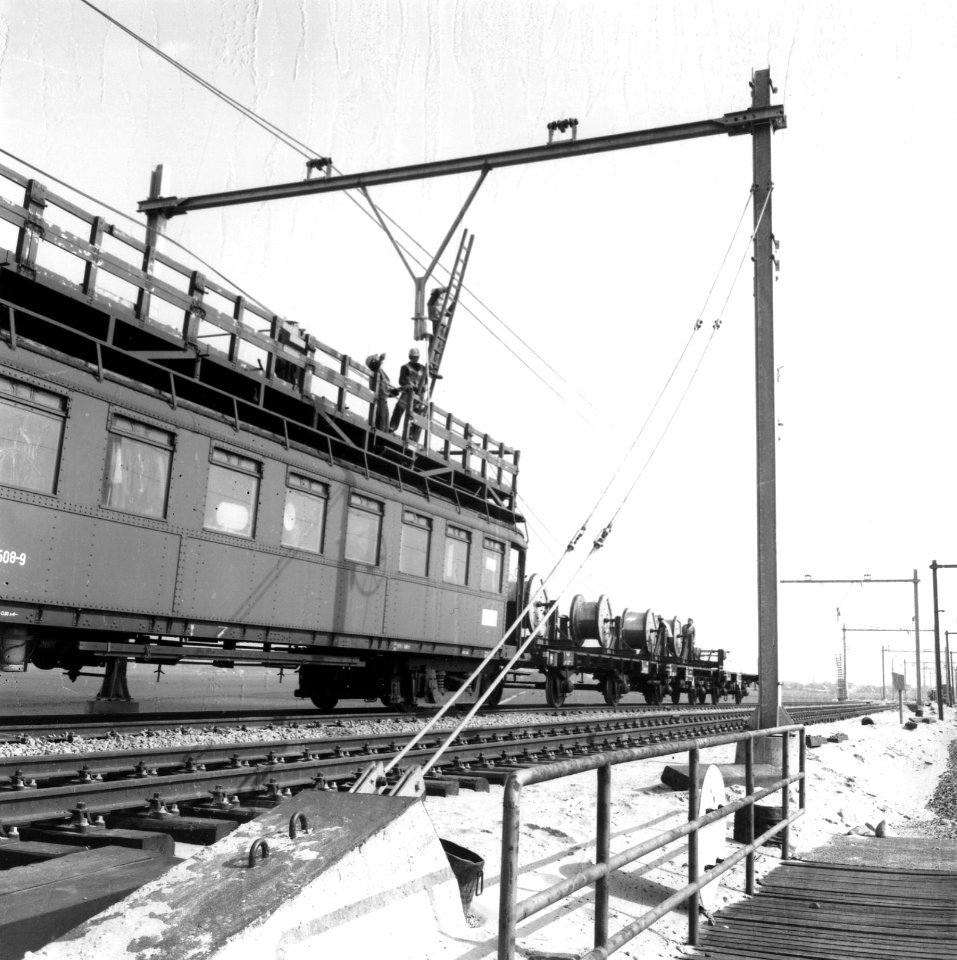 HUA-166482-Afbeelding van het aanbrengen van de bovenleiding boven een spoorlijn, met behulp van een tot montagewagen omgebouwd rijtuig mat. 1924 ("Blokkendozen") van de N.S
