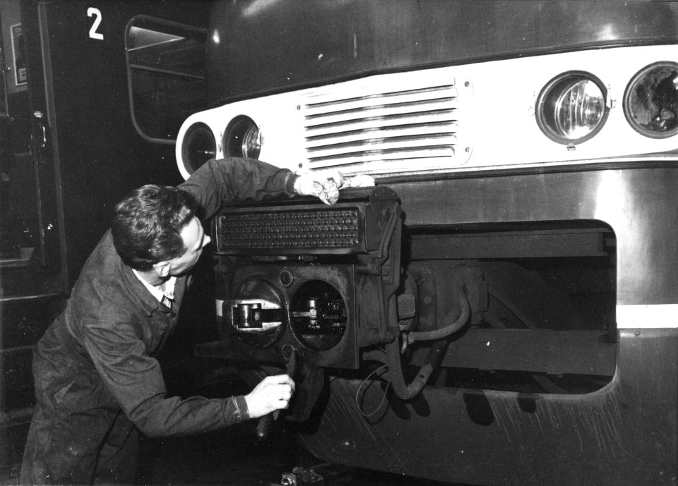 HUA-159381-Afbeelding van een onderhoudsmonteur tijdens werkzaamheden aan de automatische koppeling van een electrisch treinstel plan T (mat. 1964) van de N.S. in de lijnwerkplaats te Leidschendam