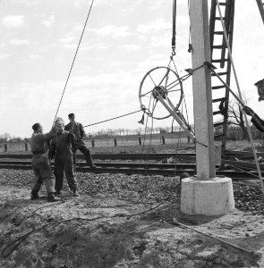 HUA-166493-Afbeelding van het plaatsen van een afspanwiel aan een bovenleidingsportaal te Wouw, tijdens de werkzaamheden ten behoeve van de electrificatie van de spoorlijn Roosendaal-Vlissingen