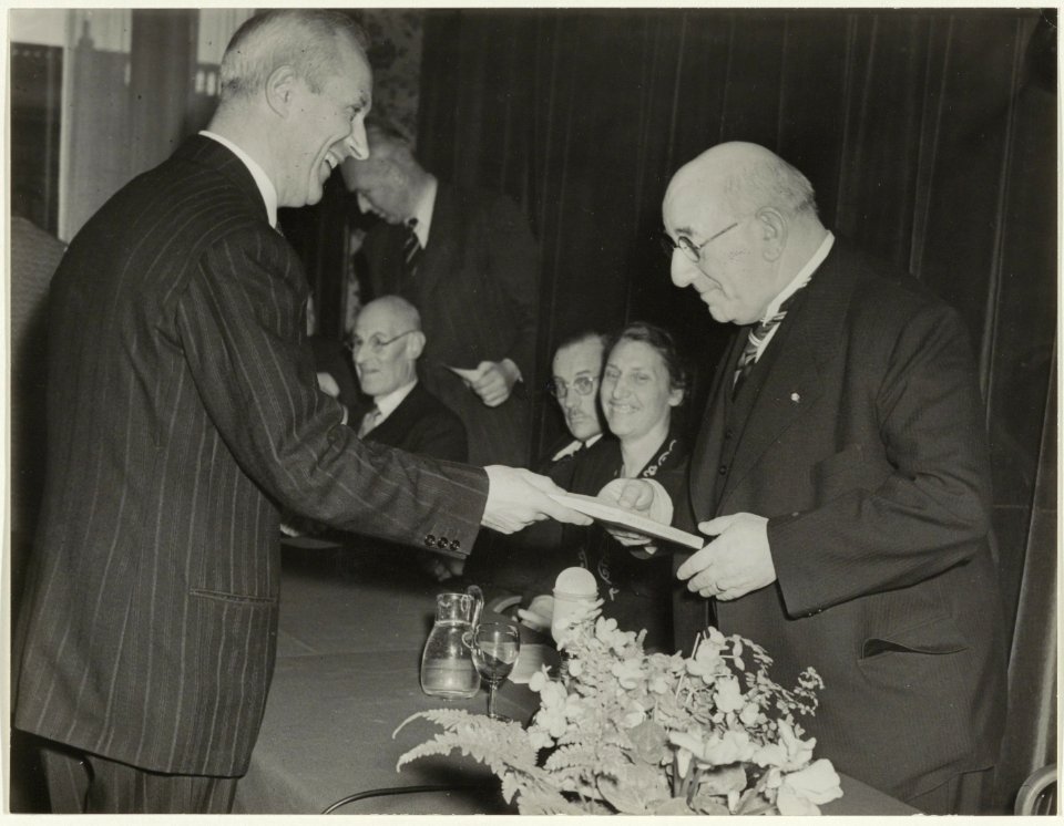 Hoofdwacht. Dr. C. Spoelder overhandigd het eerste exemplaar van de geschiedenis van de Haarlemse Hofjes, geschreven door Dr. G.h. Kurtz, aan burgemeester Cremers. NL-HlmNHA 54019340