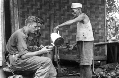 Indonesische man schenkt koffie in de mok van een soldaat. Naast hem zit een and, Bestanddeelnr 3544