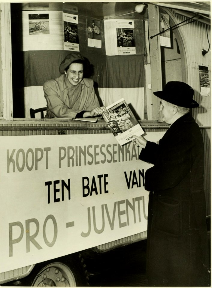 In een stand op de grote markt verkoopt mevrouw Cremers-de Bruijn Prinsessenkalenders ten bate van Pro Juventute, NL-HlmNHA 5400464771