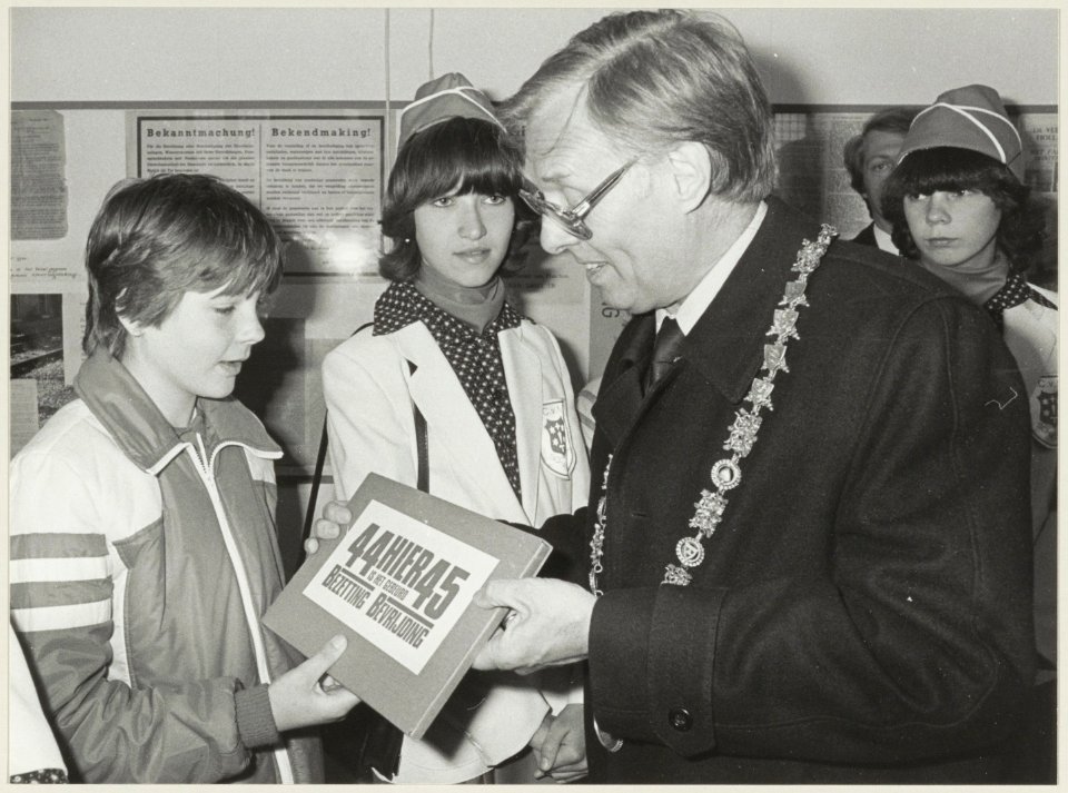 In de Vleeshal overhandigt burgemeester Reehorst documentatie aan scholieren bij de tentoonstelling over de bevrijding. NL-HlmNHA 54012602