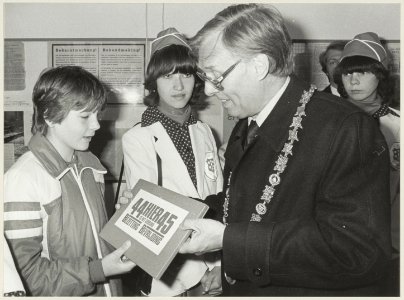 In de Vleeshal overhandigt burgemeester Reehorst documentatie aan scholieren bij de tentoonstelling over de bevrijding. NL-HlmNHA 54012602