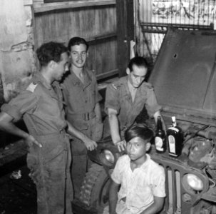 Indonesische jongen zit voor een jeep en kijkt in de lesns. Bij hem staan drie , Bestanddeelnr 6962