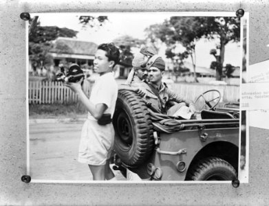 Indonesische jongeman met filmcamera bij een jeep met Brits-Indische militaire , Bestanddeelnr 901-5490