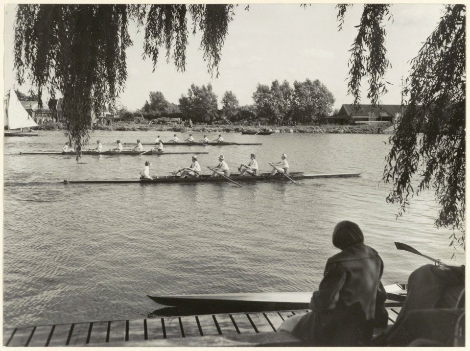 Interscholaire roeiwedstrijden op het Zuider Buitenspaarne. In de race zijn de overnaadse vier stijlroeien dames, van voor naar achter Het Kopje, M.H.B.S. en het Montessori Lyceum