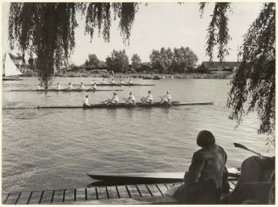 Interscholaire roeiwedstrijden op het Zuider Buitenspaarne. In de race zijn de overnaadse vier stijlroeien dames, van voor naar achter Het Kopje, M.H.B.S. en het Montessori Lyceum