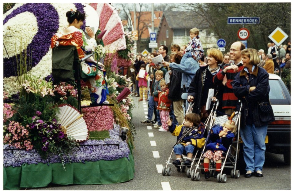 Intocht bloemencorso in Bennebroek. Marijke de Bats en Irene van der Vaart (met twee buggy's) kijken met hun kinderen hoe een drumband vrolijk misicerend Bennebroek binnen marcheert., NL-HlmNHA 54036114