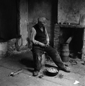 Interieur van een vervallen woning Een man schilt aardappelen, Bestanddeelnr 900-4658 photo