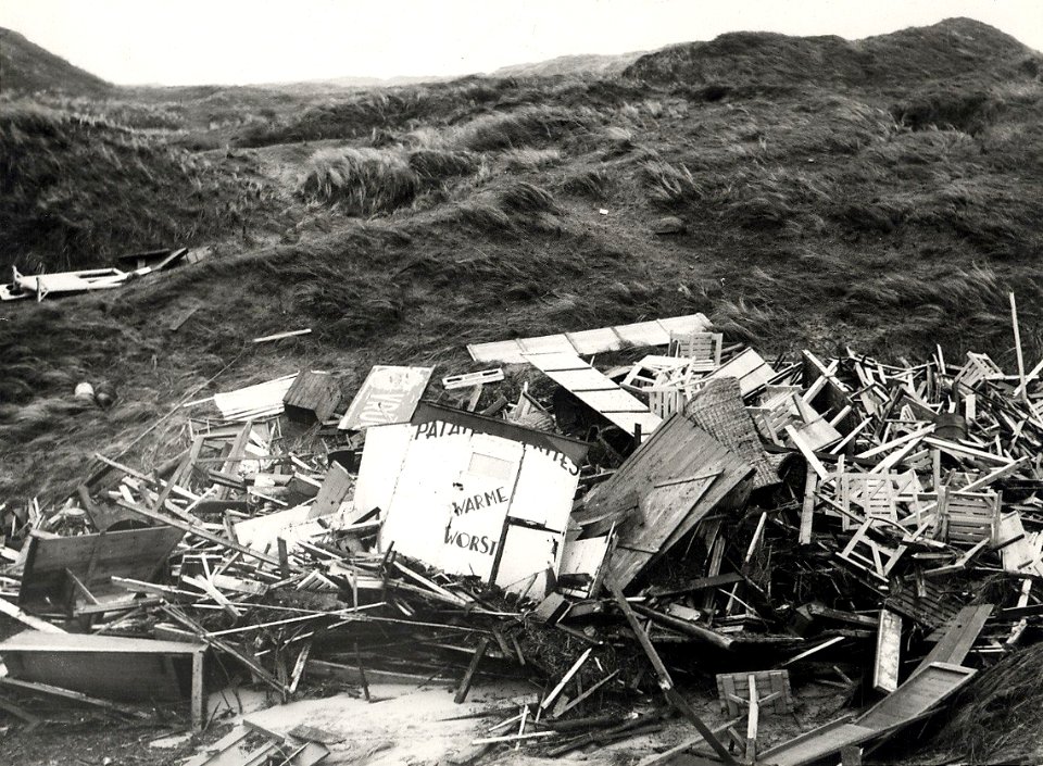 In IJmuiden werden de Consumptiekramen, die aan de voet van de Zuiderpier stonden, de duinen ingeslingerd door de storm. Aangekocht in 1976 van fotograaf C. de Boer. Identificatienummer 54-0, NL-HlmNHA 1478 25900 K 38
