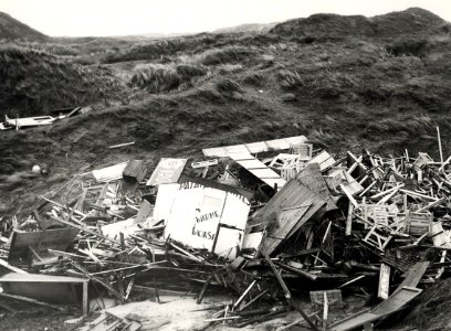 In IJmuiden werden de Consumptiekramen, die aan de voet van de Zuiderpier stonden, de duinen ingeslingerd door de storm. Aangekocht in 1976 van fotograaf C. de Boer. Identificatienummer 54-0, NL-HlmNHA 1478 25900 K 38