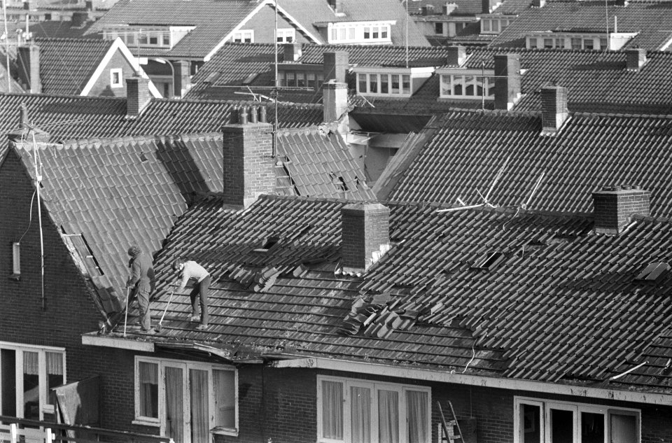 Iemand staat op het beschadigde dak van een woning, Bestanddeelnr 926-9323
