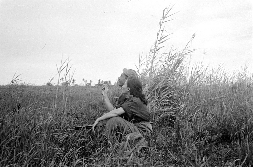 Jonge vrouw en Indonesische man in uniform zitten naast elkaar in een veld. De m, Bestanddeelnr 6092