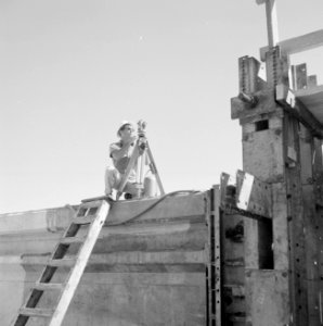 Jongeman op een verhoging van het bouwterrein met een landmeter, Bestanddeelnr 255-2560
