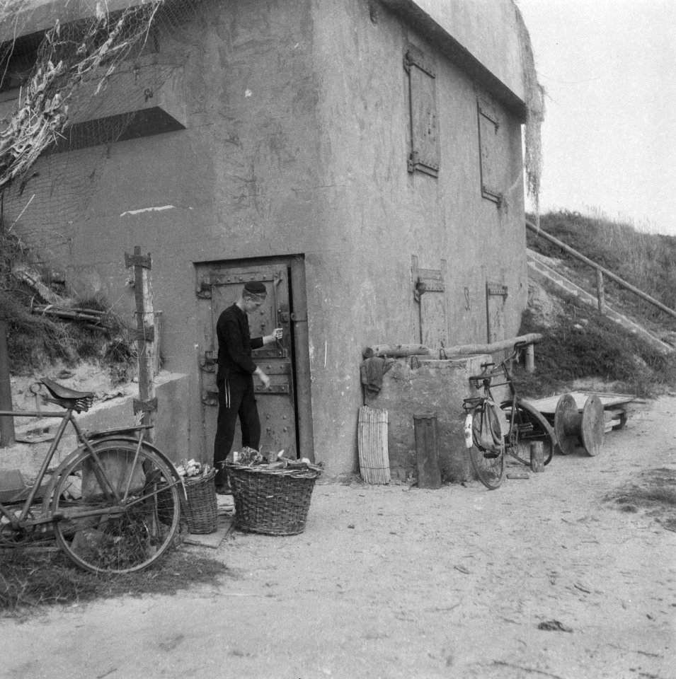 Jongeman bij de deur van een vormalige Duitse bunker, Bestanddeelnr 900-7576