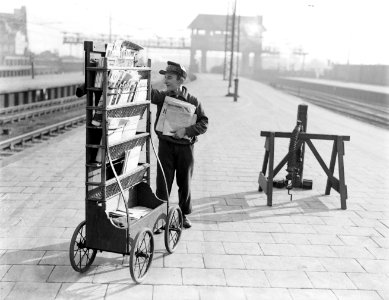 Jonge tijdschriftenverkoper van de AKO staand bij mobiele kiosk op perron, Bestanddeelnr 252-1068