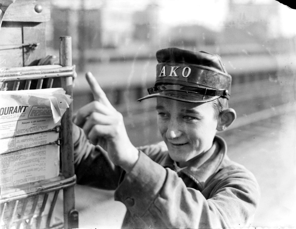 Jonge tijdschriftenverkoper van de AKO wijst bij mobiele kiosk, Bestanddeelnr 252-1067
