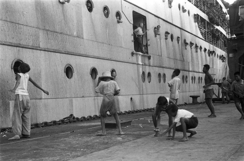 Jongens aan de kade vangen snoepgoed en sigaretten op die vanaf het schip worde…, Bestanddeelnr 82-3-1