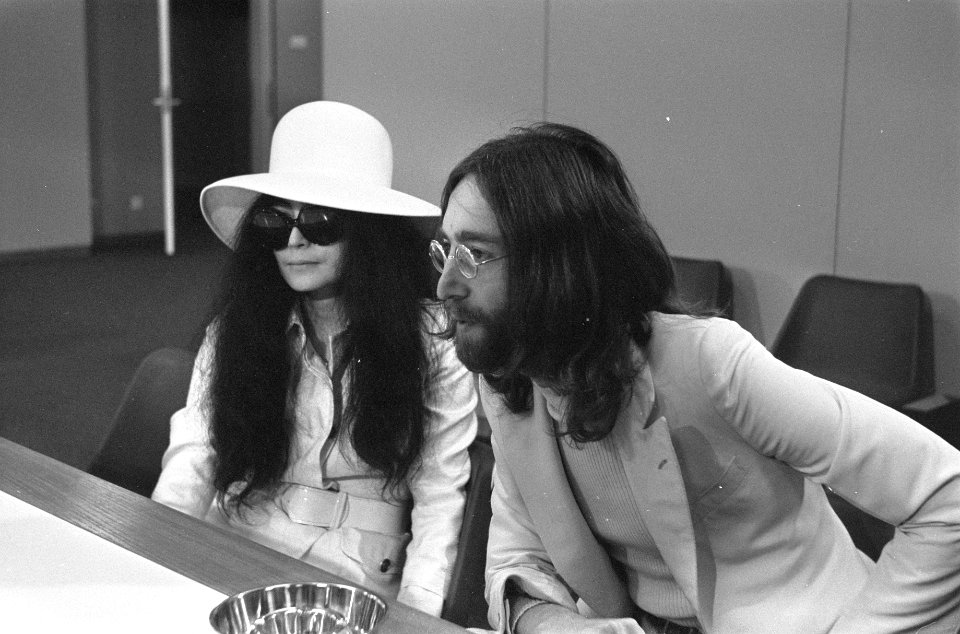 John Lennon en echtgenote Yoko Ono vertrekken van Schiphol naar Wenen in de vert, Bestanddeelnr 922-2496