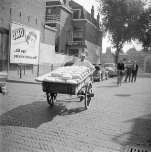 Kaashandelaar met een lading kaas op de achtergrond een reclamebord voor Omo, Bestanddeelnr 254-4069