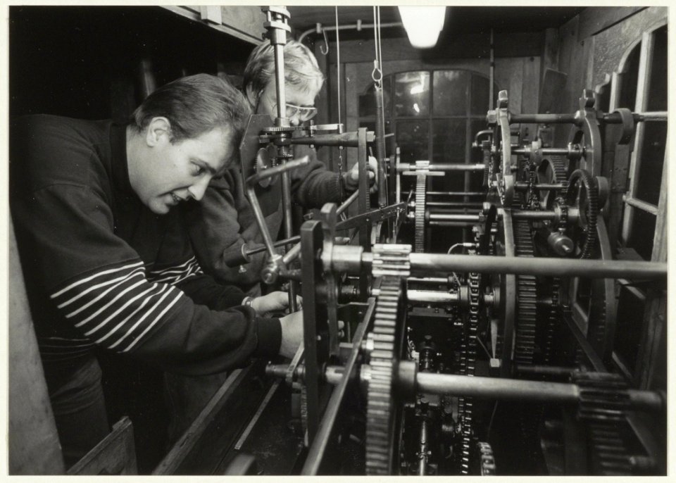 Jeffrey Keur (links) en Bert van Veldhuijsen werken aan het uurwerk van de Grote of St Bavokerk. NL-HlmNHA 54032074