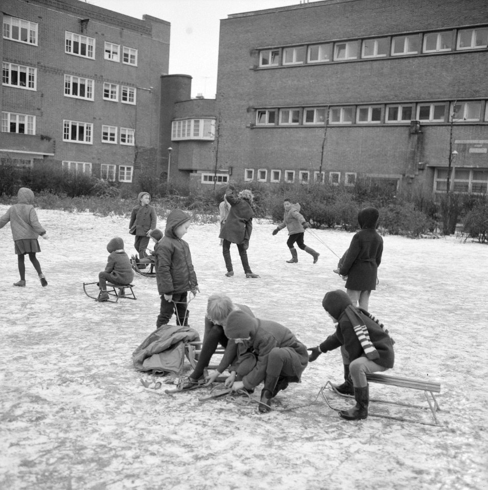 Kinderen bij het onderbinden van hun schaatsen, zittend op sleetjes op het ijs, Bestanddeelnr 918-4690