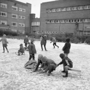 Kinderen bij het onderbinden van hun schaatsen, zittend op sleetjes op het ijs, Bestanddeelnr 918-4690